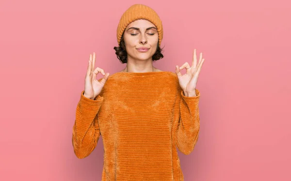 カジュアルな服とウールキャップを身に着けている若いヒスパニック系の女性は 指で瞑想のジェスチャーを行う閉じて目でリラックスして笑顔 ヨガのコンセプト — ストック写真