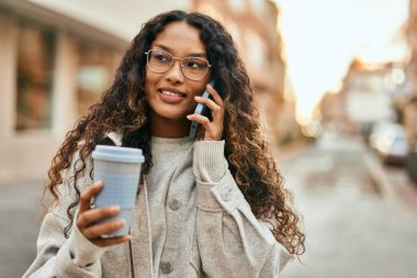 Genç Latin kadın akıllı telefondan konuşuyor ve şehirde kahve içiyor..