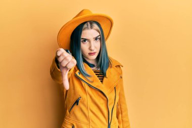 Sarı şapka ve deri ceket giyen genç modern bir kız mutsuz ve kızgın görünüyor. Reddedilmiş ve olumsuz bir hareket sergiliyor. kötü ifade. 