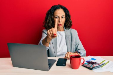 Ofiste çalışan orta yaşlı güzel bir kadın bir fincan kahve içip parmağını kaldırmış ve kızgın bir ifade takınıyor. 