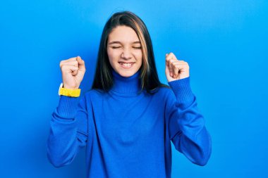 Balıkçı yaka kazak giyen genç esmer kız başarı için heyecanlanıyor kolları havada ve gözleri kapalı zaferi kutluyor. Kazanan konsept. 