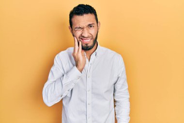 Sakallı, iş gömleği giyen İspanyol bir adam diş ağrısı ya da diş hastalığından dolayı acı dolu bir ifadeyle ağzına dokunuyor. dişçi 