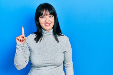 Genç İspanyol kadın gündelik kıyafetler giyip bir numarayı gösterip işaret ederken kendinden emin ve mutlu bir şekilde gülümsüyor.. 