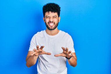 Sakallı, beyaz tişörtlü, komik gülümseyen genç bir Arap adam kedi gibi pençe hareketi yapıyor, agresif ve seksi bir ifade. 