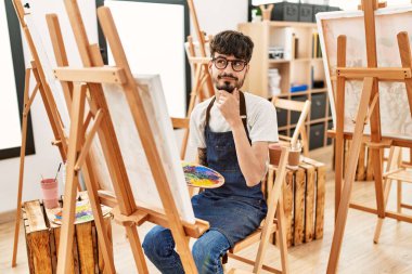 Resim stüdyosunda sakallı İspanyol bir adam ciddi bir yüz ifadesi olan eli çenesinde soru soran kafa karıştırıcı bir fikir hakkında düşünceli bir adam. 