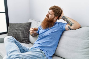 Genç İrlandalı adam evdeki kanepede çay içiyor..