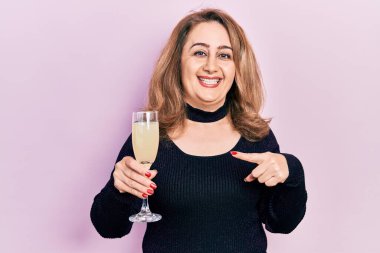 Orta yaşlı beyaz kadın bir bardak şampanya içiyor mutlu bir şekilde el ve parmak işareti yapıyor. 