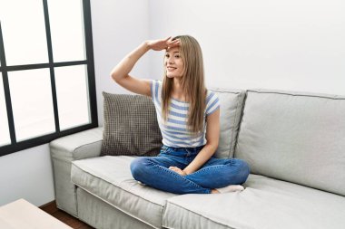 Asyalı genç bir kadın evdeki kanepede oturuyor. Çok mutlu ve gülümsüyor. Çok uzaklara bakıyor. arama kavramı. 