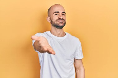 Genç kel bir adam, günlük beyaz tişört giyiyor. Gülümsüyor. Avuç içi dolusu yardım eli uzatıyor ve kabul ediyor.. 