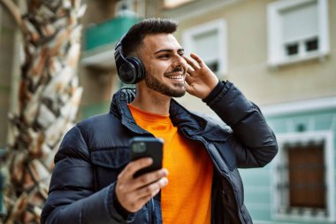 Yakışıklı, sakallı, neşeli, kendine güvenen, kışlık palto giyen, akıllı telefondan müzik dinleyen bir İspanyol.