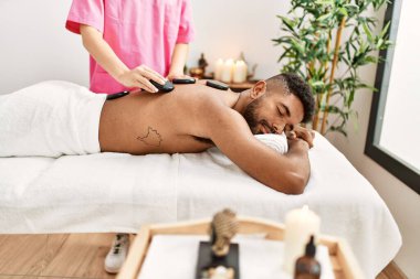 Güzellik merkezinde siyah taşlarla masaj yaptıran adam..