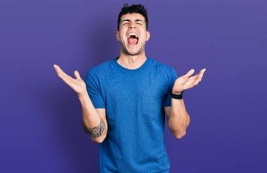 Gündelik tişört giyen genç İspanyol adam başarı için deli ve çılgınlığı kutluyor kollarını kaldırmış ve gözlerini kapatmış heyecanla bağırıyor. Kazanan konsept 