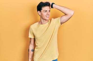 Günlük sarı tişört giyen genç İspanyol adam gülümsüyor saçlara dokunuyor, el hareketi yapıyor, çekici ve modaya uygun poz veriyor. 