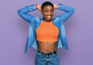 Genç Afro-Amerikalı kadın günlük kıyafetler giyiyor rahatlıyor ve esniyor, kolları ve elleri başının arkasında mutlu bir şekilde gülümsüyor. 