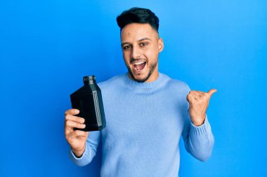 Genç Arap adam motor yağı şişesini tutarken baş parmağını yana kaldırıyor ve ağzı açık gülümsüyor. 