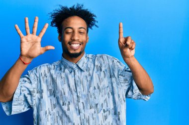 Sakallı, genç, Afro-Amerikan bir adam. Altı numaralı parmaklarıyla kendini beğenmiş ve mutlu gülümserken kendini belli ediyor.. 