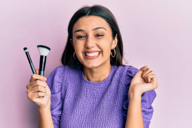 Makyaj fırçaları tutan genç İspanyol kadın gururla haykırıyor, zaferi ve başarıyı kutluyor. 