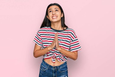 Gündelik giysiler giyen genç İspanyol kız elleri ile yalvarıyor ve dua ediyor. Yüzünde umut ifadesi var. Çok duygusal ve endişeli. Yalvarıyor. 