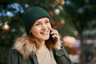 Beyaz kız gülümsüyor. Parktaki akıllı telefondan konuşuyor.