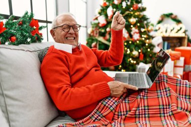 Yılbaşı ağacının yanında dizüstü bilgisayar kullanarak oturan yaşlı adam öfkeyle bağırıyor, öfkeyle bağırıyor ve el kaldırıyor. 