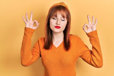 Kızıl saçlı, turuncu süveter giyen genç kadın rahatla ve gülümse gözleri kapalı parmaklarıyla meditasyon hareketi yapıyor. yoga konsepti. 