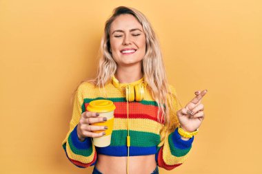 Güzel sarışın kadın, kulaklık takarak kahve içiyor. Umut ve gözlerin kapalı bir şekilde gülümseyerek işaret ediyor. Şans ve batıl inançlar. 