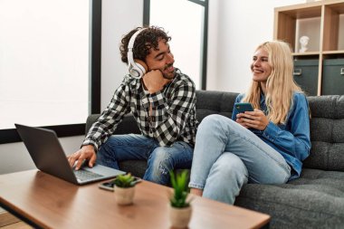 Evde dizüstü bilgisayar ve akıllı telefon kullanan genç çift mutlu..
