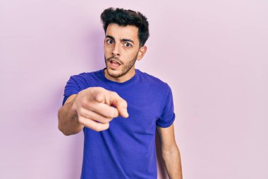 Gündelik tişört giyen genç İspanyol adam kameraya kızgın ve sinirli bir şekilde seni işaret ediyor. 
