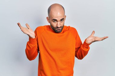 Gündelik kıyafetler giyen genç kel adam habersiz ve kolları açık, hiçbir fikri ve şüpheli bir yüzü var.. 