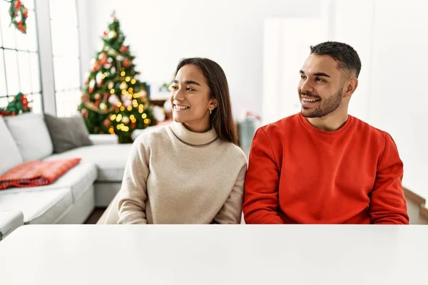 他那对年轻的惊慌失措的夫妇坐在桌子旁 坐在圣诞树旁 望着旁边 脸上挂着微笑 表情自然 充满自信地大笑 — 图库照片