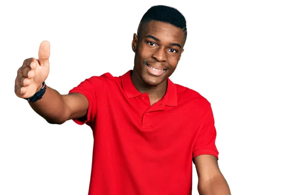 カジュアルな赤いTシャツを着た若いアフリカ系アメリカ人の男性が 抱擁のために腕を広げて笑顔でカメラを見ている 幸せを受け入れる陽気な表情 — ストック写真