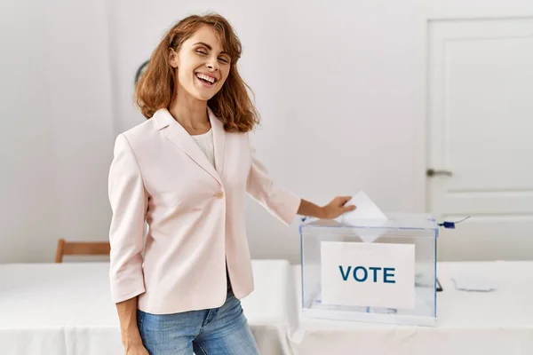 Young caucasian voter woman smiling happy putting vote in ballot box at electoral college.