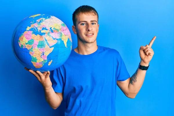 Ung Kaukasier Man Håller Världen Bollen Ler Glad Pekar Med — Stockfoto