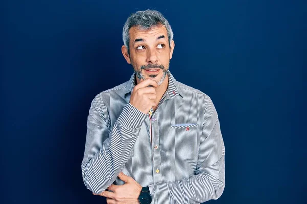 質問について考える顎の手でビジネスシャツを身に着けている灰色の髪を持つハンサムな中年の男 集中的な表現 思慮深い顔で笑顔 疑わしい概念 — ストック写真