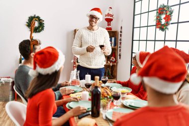 Mutlu bir şekilde gülümseyen bir grup genç Noel yemeği yiyor ve evde kadeh kaldırıyor..