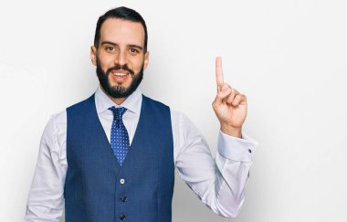 Sakallı, iş yeleği giyen bir numaralı parmağını gösterip gülümseyen, kendinden emin ve mutlu bir genç.. 