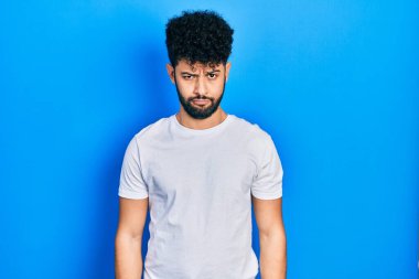 Sakallı, sıradan, beyaz tişörtlü, kuşkucu ve gergin genç bir Arap, sorun yüzünden surat asıyor. negatif kişi. 