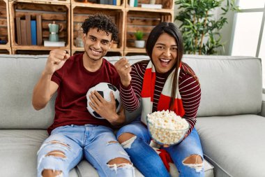 Evdeki kanepede oturan genç latin çift futbol maçını izliyor ve destekliyor..