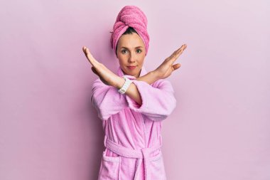 Banyo havlusu şapkası ve bornoz reaksiyonu takan genç sarışın kadın kollarını kavuşturup, avuç içlerini bozarken kızgın surat ifadesi takınıyor. 