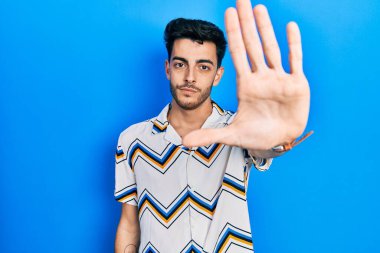 Günlük kıyafetler giyen genç İspanyol adam avucunun içi gibi şarkı söylemeyi kesiyor. Yüzünde olumsuz ve ciddi bir jest olan uyarı ifadesi. 