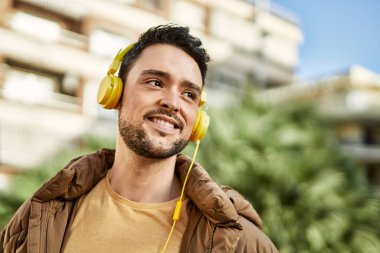 Şehirde kulaklık takarak mutlu gülümseyen genç İspanyol adam..