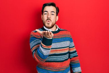 Sakallı, zarif yün kazak giyen yakışıklı beyaz bir adam kameraya bakıp havada el sallayarak öpüşüyor ve çok güzel ve seksi. aşk ifadesi. 