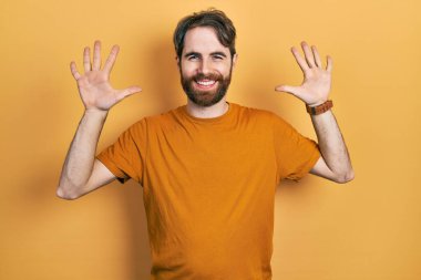 Sakallı, sıradan sarı tişörtlü beyaz bir adam on numarayı gösteriyor ve gülümsüyor. Kendinden emin ve mutlu.. 