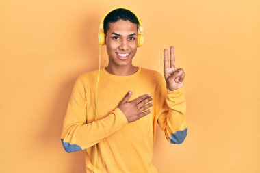 Genç Afro-Amerikalı adam kulaklık takarak müzik dinliyor. Gülümsüyor, yemin ediyor, el pençe divan duruyor. 