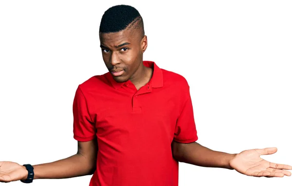 身穿休闲红T恤的年轻的非洲裔美国人 毫无头绪 与张开双臂混淆不清 没有概念 — 图库照片