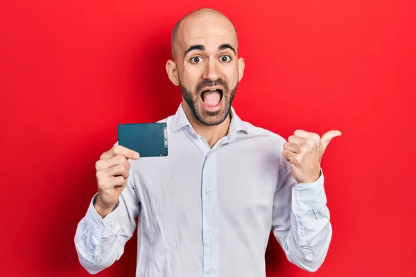 Young Bald Man Holding Ssd Memory Pointing Thumb Side Smiling — Stock Photo, Image