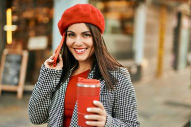 Genç İspanyol kadın akıllı telefondan konuşuyor ve şehirde kahve içiyor..