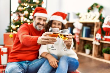 Orta yaşlı İspanyol çift Noel şapkası takıyor. Yerde oturup evde şampanyayla kadeh kaldırıyorum..