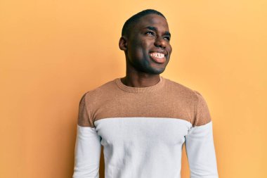 Genç Afro-Amerikan bir adam günlük kıyafetler giyip yüzünde gülümseme, doğal bir ifade ile yan yana bakıyor. Kendinden emin gülen. 