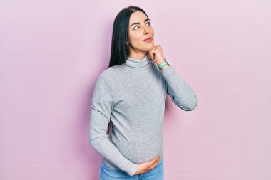 Mavi gözlü güzel bir kadın bebek bekliyor, eli çenesinde hamile karnına dokunuyor soru soruyor, düşünceli bir yüz ifadesi var. Düşünceli bir yüzle gülümsüyor. şüphe kavramı. 